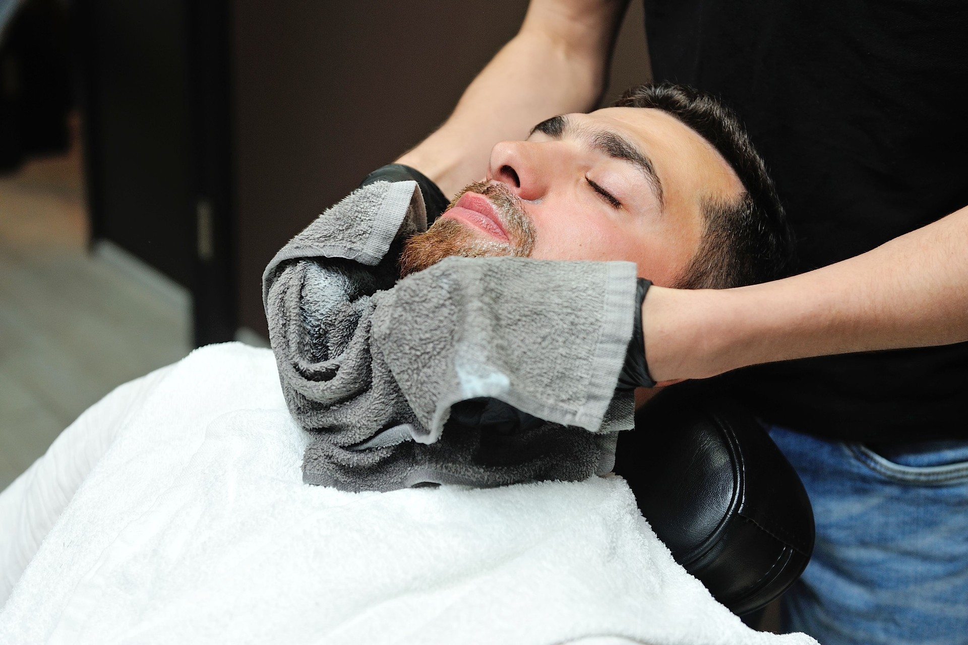 Barber preparing man face for shaving with hot towel