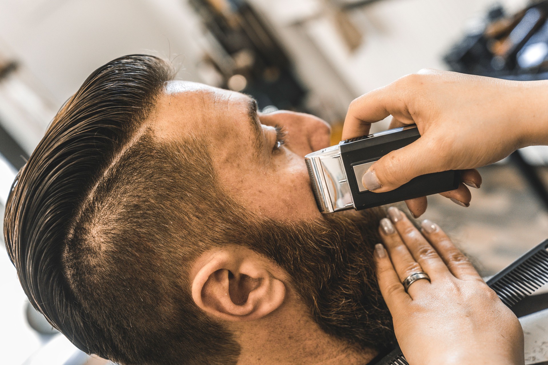 Hipster man at barbershop salon getting beard and hair cut - Hairdresser woman using electric razor for beard trimming - Barber shop concept